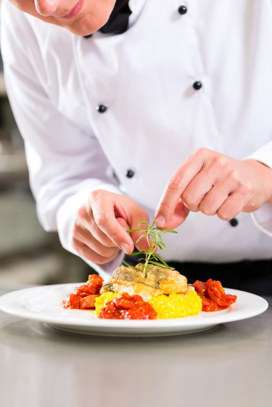 Chef in hotel or restaurant kitchen cooking, he is finishing a dish on plate